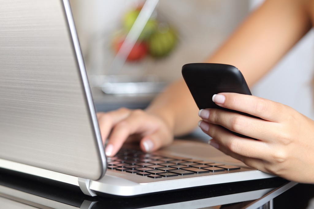 Woman hand using a smart phone and typing a laptop at home