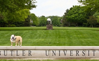 The Butler bulldog stands atop the Butler University sign, with a large grass field in the background.