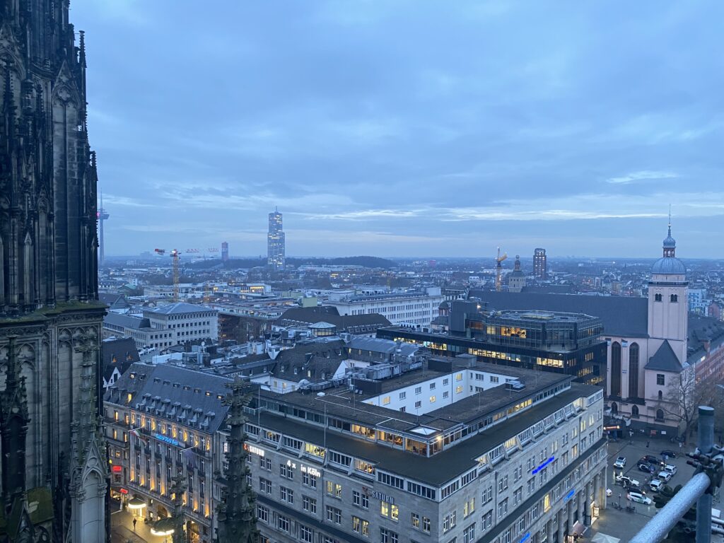 View of Cologne from the Cologne Cathedral, in the distance there is a large skyscraper. In the foreground is more Baroque architecture