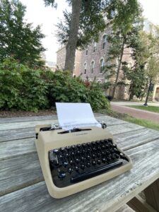 Typewriter on picnic table with trees and stone building in the background
