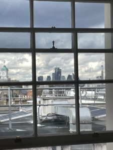 Skyscrapers in distance, industrial rooftops in foreground, viewed through a paned window