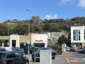 Nando's restaurant in shopping center with wooded ridge behind topped by Dover Castle